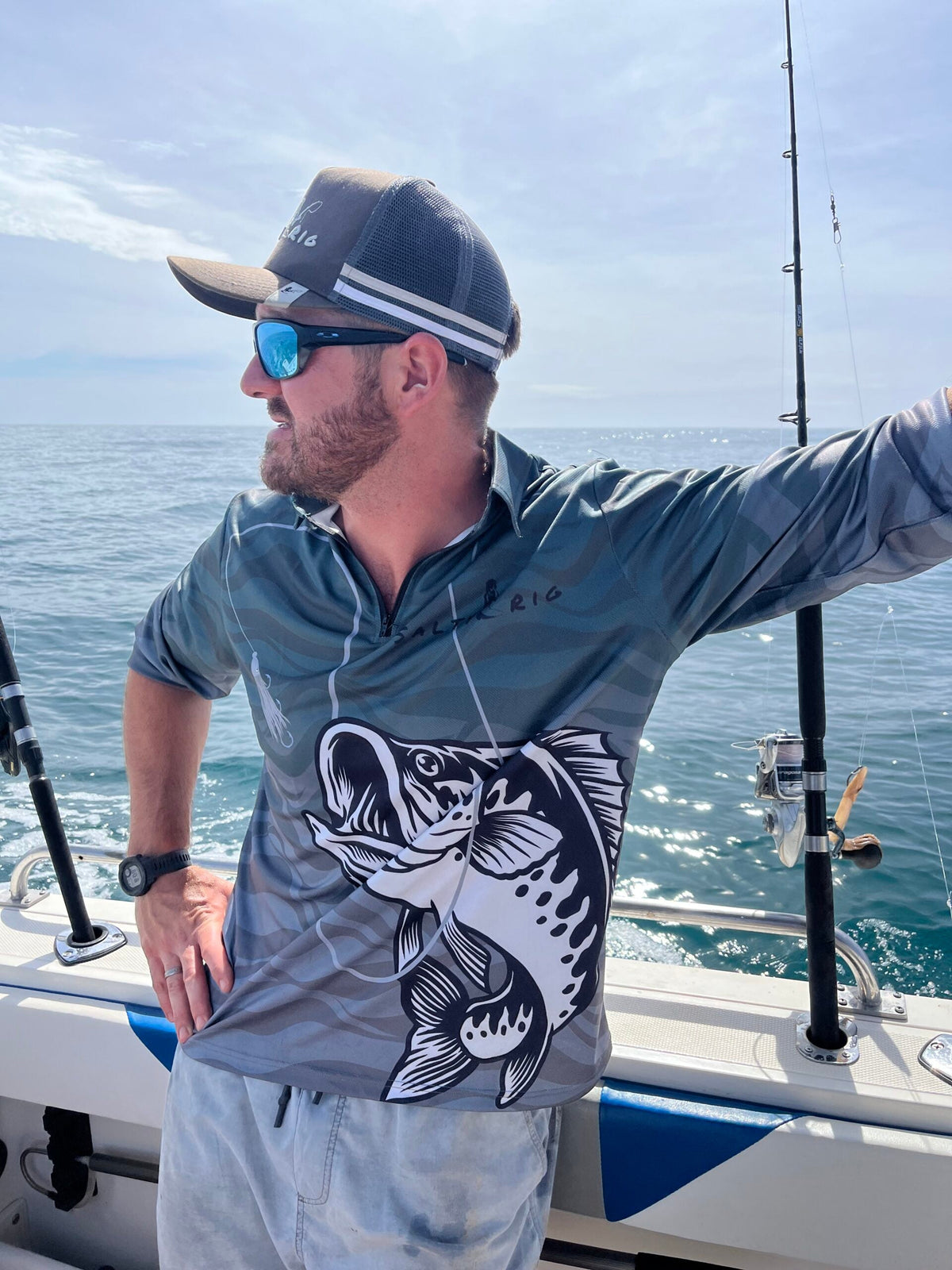 Man on a boat wearing a fishing shirt with a fish design, surrounded by water and clear sky.
