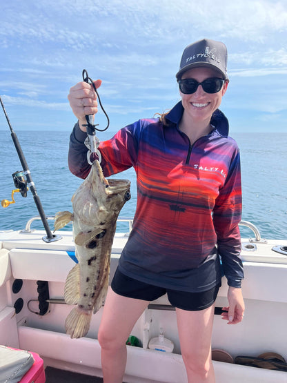 Person holding a fish on a boat with a blue sky and ocean background