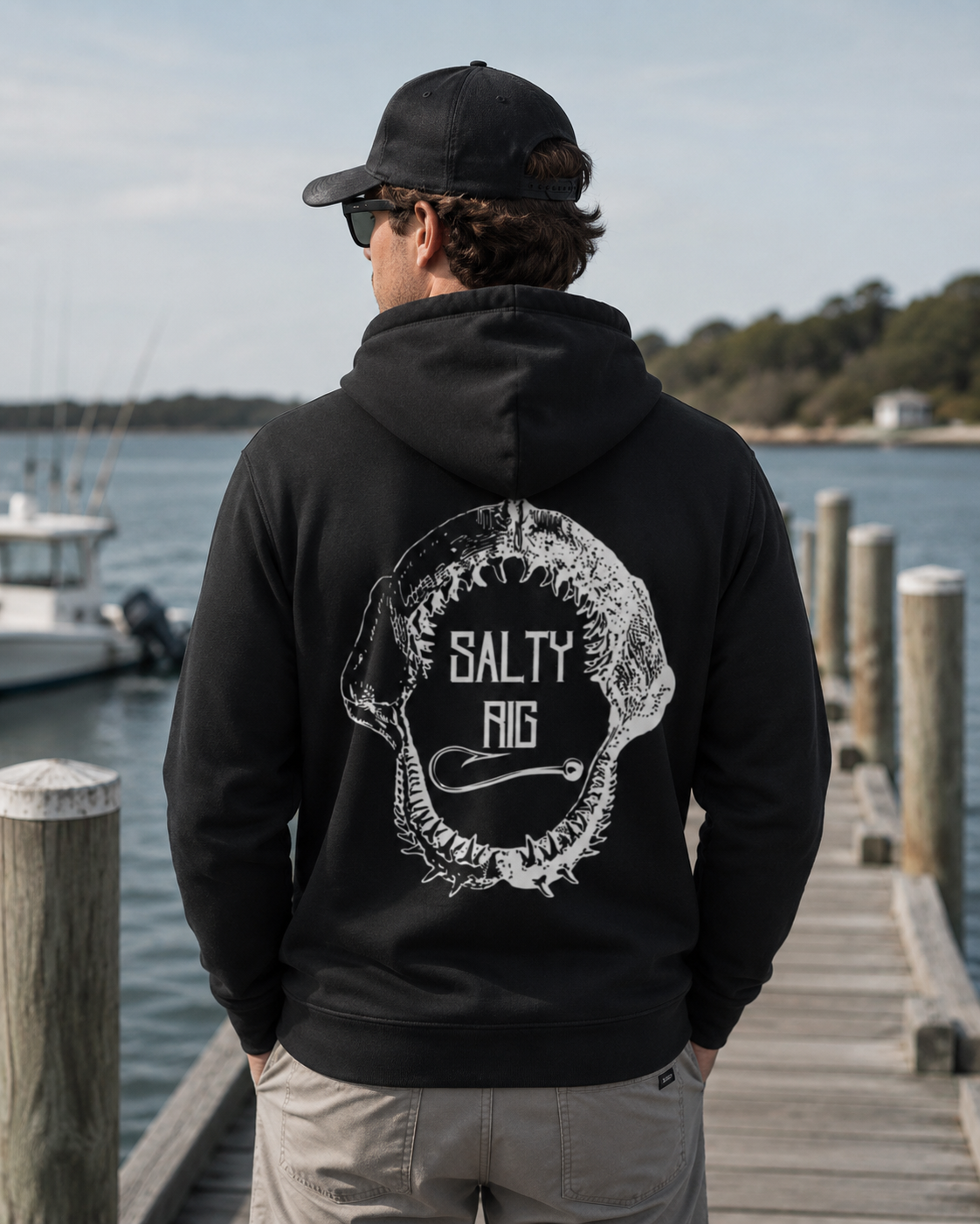 Person wearing a black hoodie with 'Salty Rig' logo on a dock by water