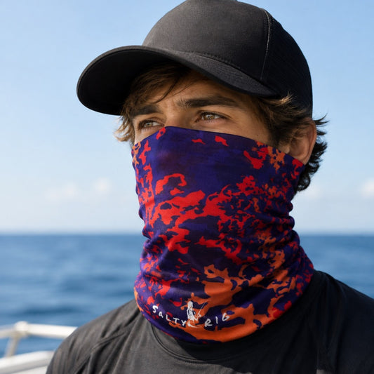 A man wearing a black baseball cap and a dark gray t-shirt, with a blue and red camouflage patterned neck gaiter pulled up over his nose and mouth. The gaiter features the white printed brand name 'SALTY 216' near the bottom.