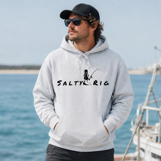 A man wearing a light gray heather hoodie with a black 'SALTY RIG' fishing graphic stands by the ocean, wearing a black cap and sunglasses.